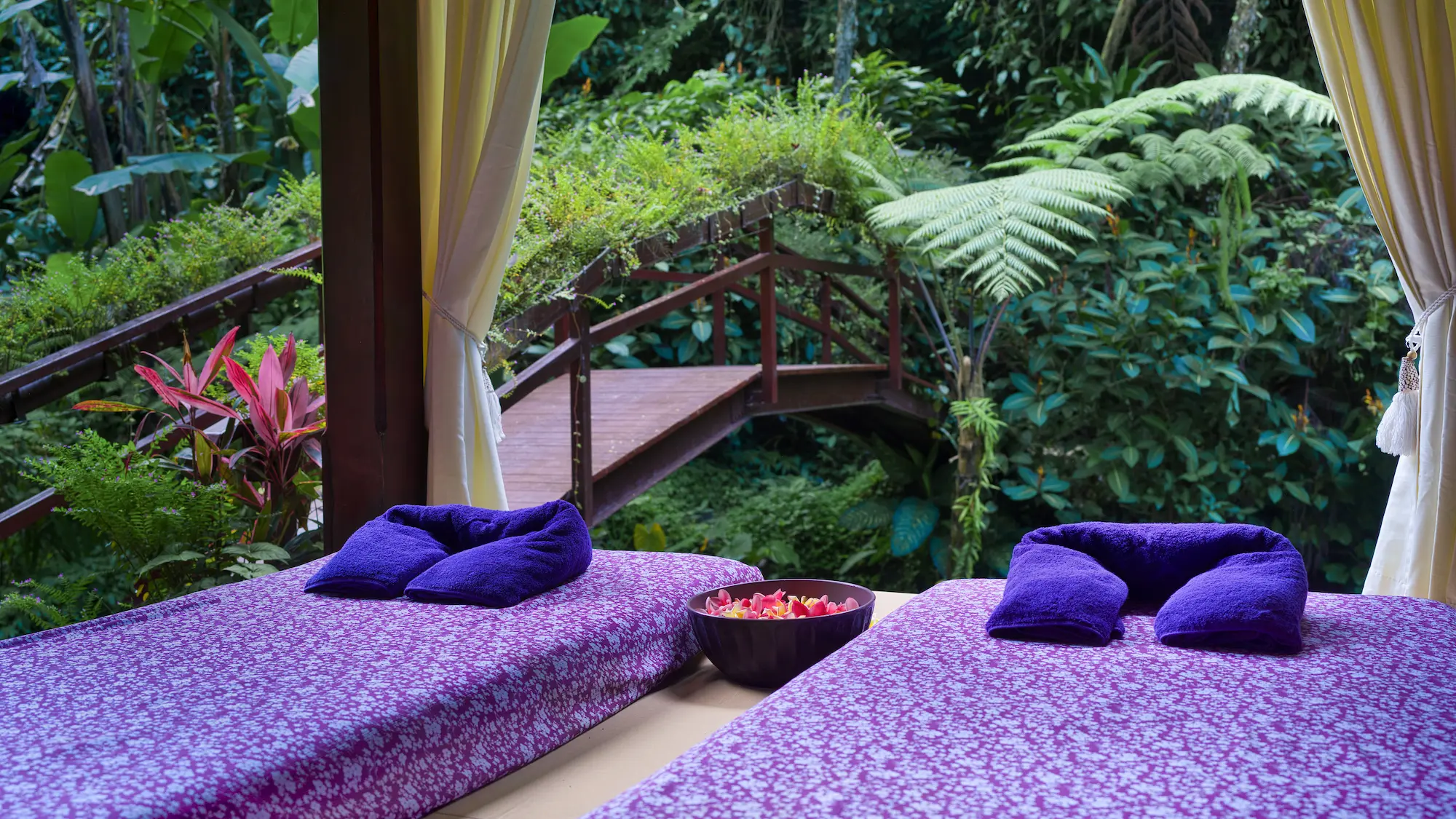 Couple enjoying a luxury spa retreat in Bali with a private riverside pavilion and romantic flower bath experience surrounded by jungle views.